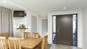 Un comedor con una mesa y sillas de madera, un jarrón con flores y una puerta de madera oscura.