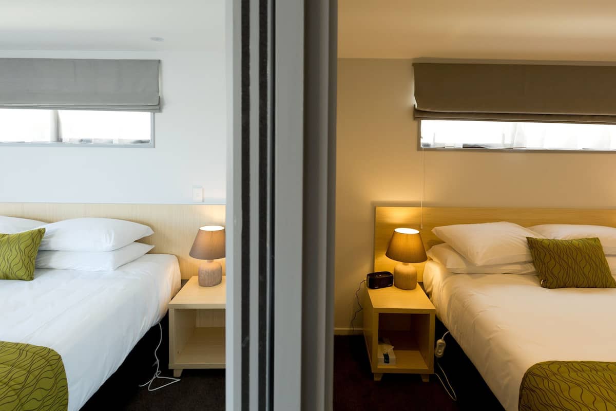 A hotel room with two beds, bedside tables, lamps, and a window with a view.
