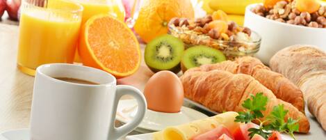 Een ontbijttafel met sinaasappelsap, een kop koffie, croissants, eieren en vers fruit.