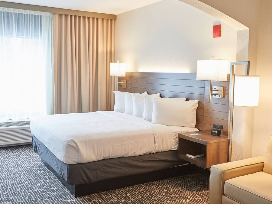 A hotel room with a large bed, bedside lamps, a nightstand, a chair, and a window with curtains.