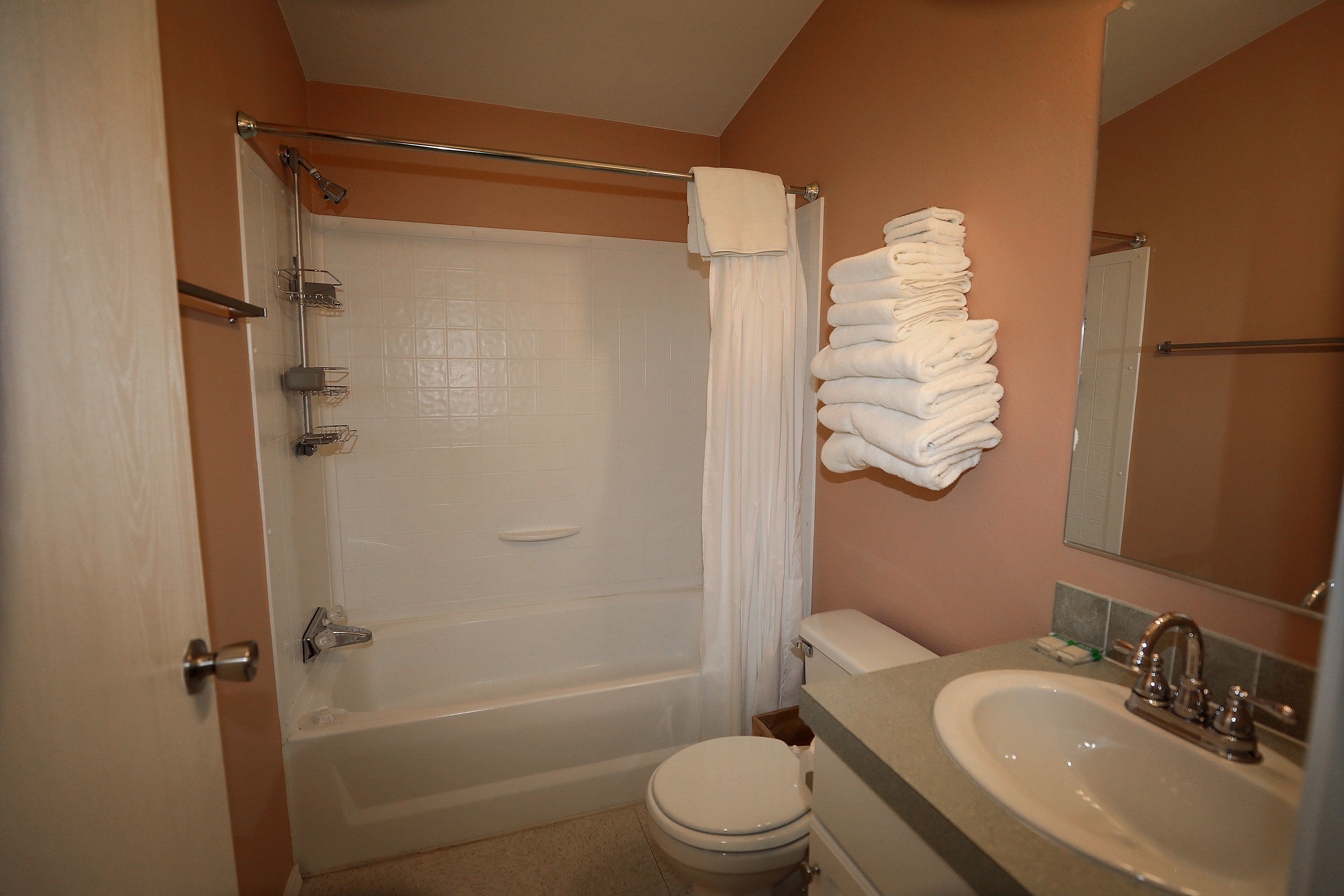 A bathroom with a bathtub, toilet, sink, and a towel rack with folded towels.