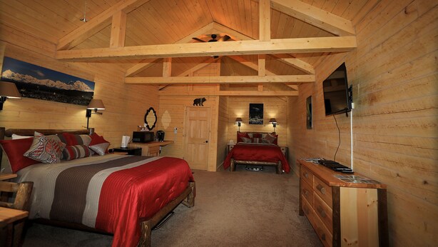 Ein Schlafzimmer in einer Blockhütte mit zwei Betten, einem Holzkleiderschrank und einem an der Wand befestigten Fernseher.