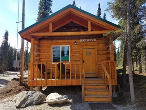Una cabaña de madera llamada Caribou, con techo verde, una ventana y una puerta.