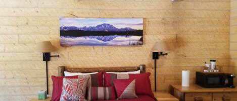 A wooden-paneled bedroom with a bed, two bedside tables, a nightstand, a lamp, a painting, and a microwave.