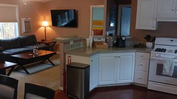 Un espacio habitable compacto con kitchenette, un sofá, una mesa de centro y un televisor montado en la pared.