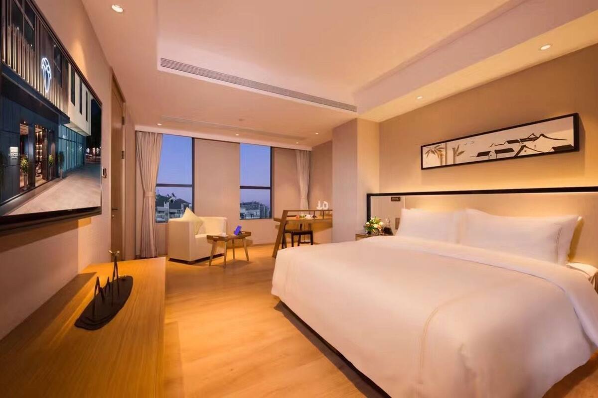 Quarto de hotel com uma cama grande, uma escrivaninha, uma cadeira, uma televisão e vista para a cidade.