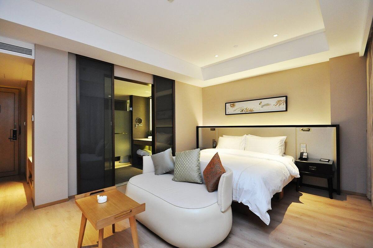 Quarto de hotel moderno com uma cama grande, uma mesa de cabeceira, uma pequena mesa de madeira e um closet espaçoso.