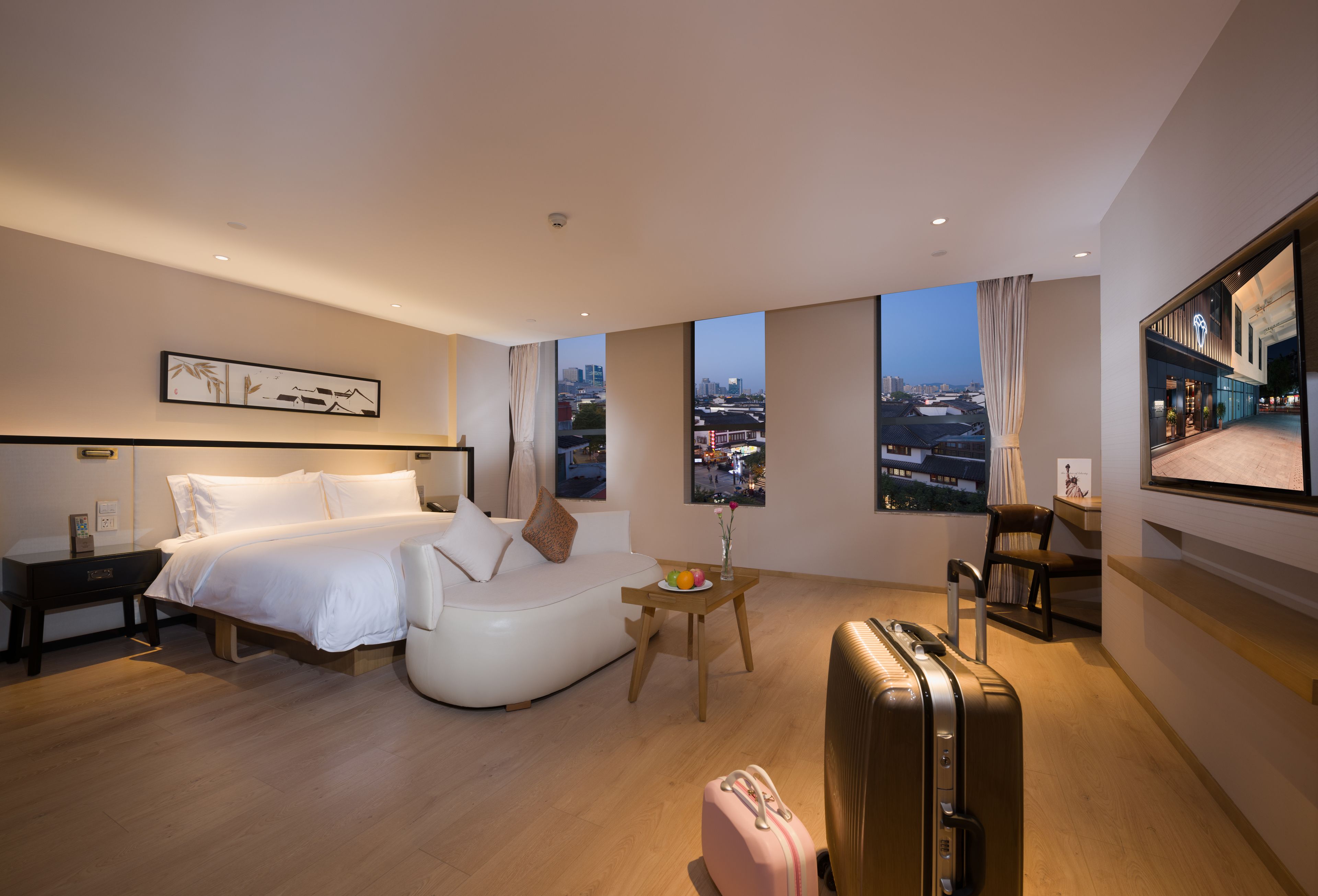 Een moderne hotelkamer met een bed, een bank, een kleine tafel met een vaas en een koffer.