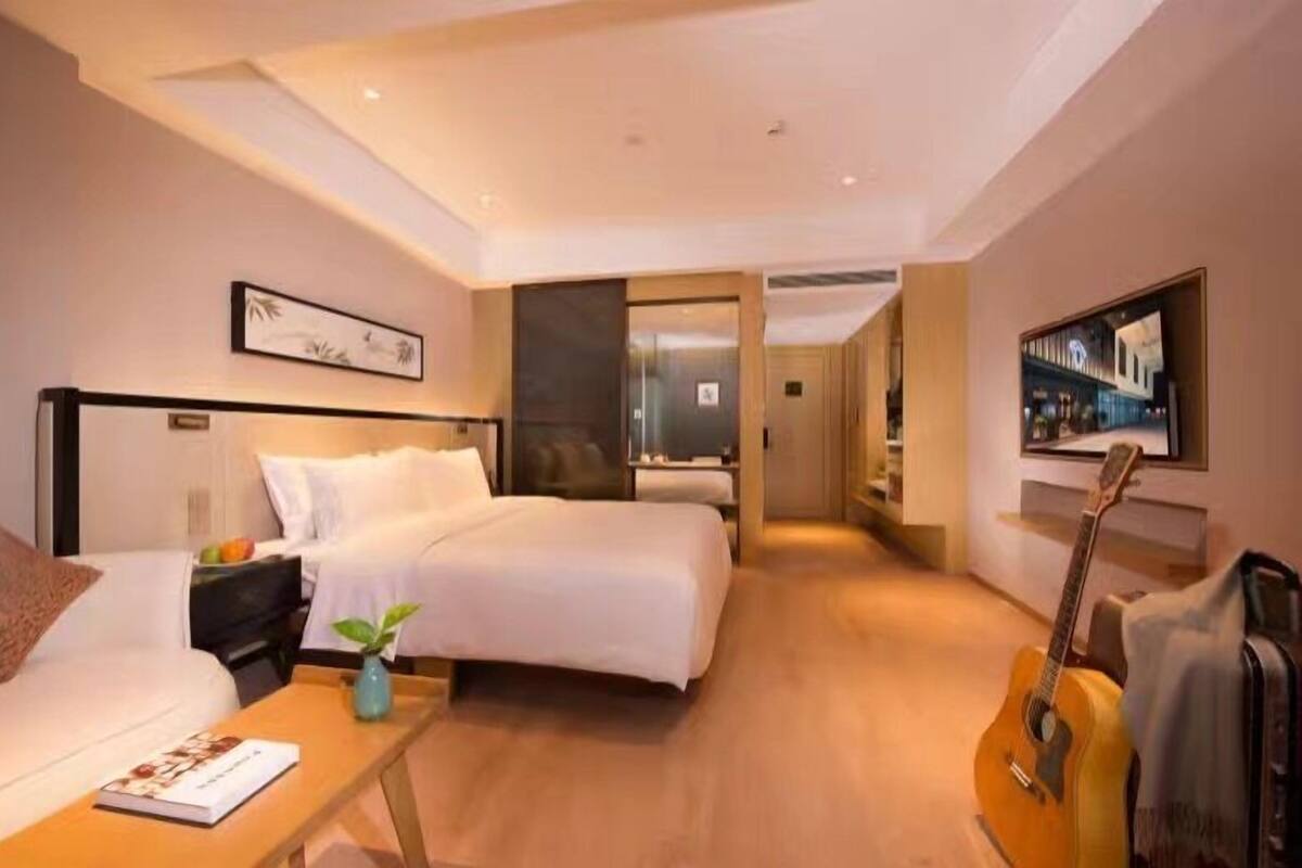 Quarto de hotel com cama, escrivaninha, guitarra e televisão.