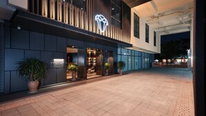 Ein modernes Hotel mit einer auffälligen Neonreklame, großen Fenstern und Pflanzkübeln im Eingangsbereich.
