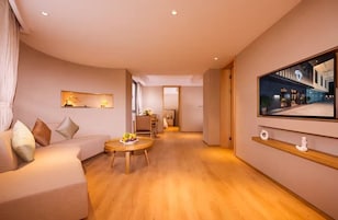 Una sala de estar moderna con un sofá, una mesa de centro redonda de madera y un televisor de pantalla plana grande montado en la pared.