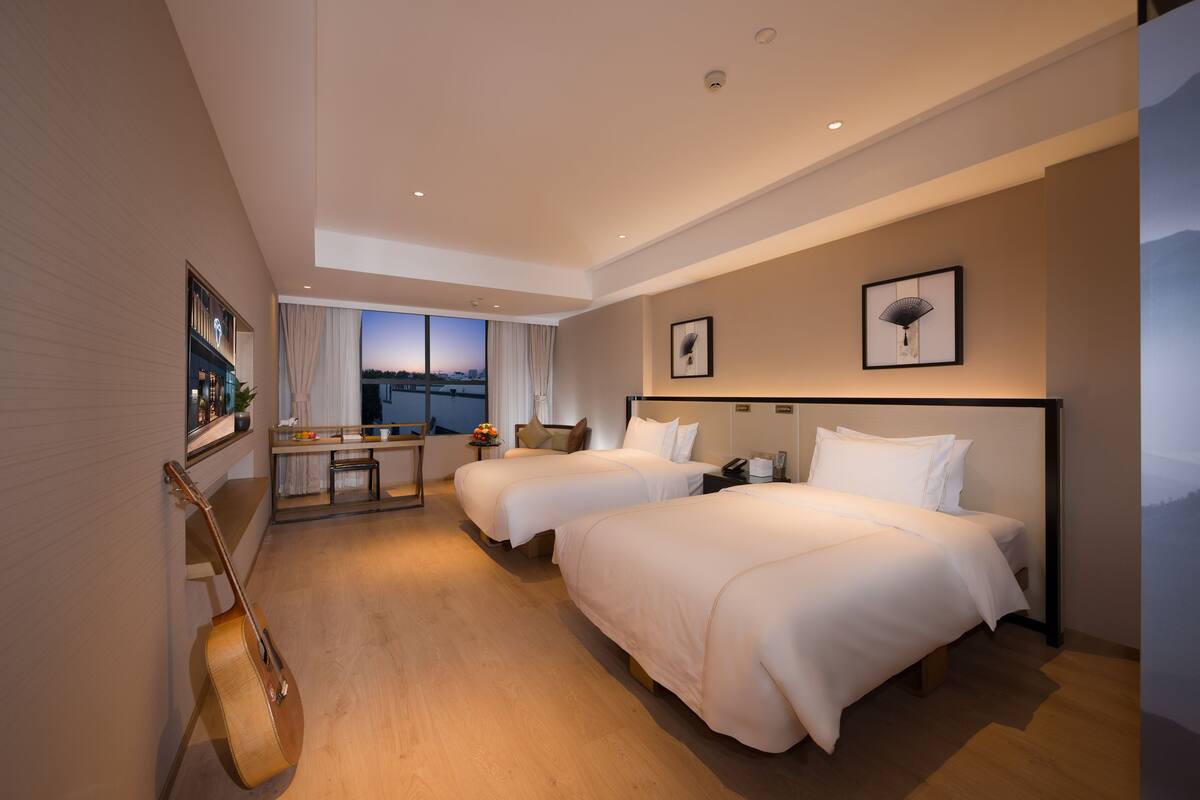 Quarto de hotel moderno com duas camas, uma escrivaninha e um violão.