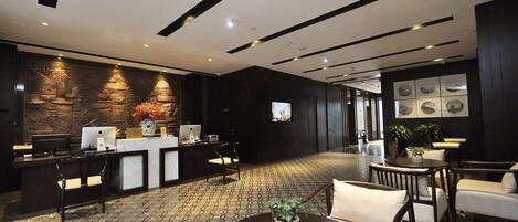 Un hall d’hôtel moderne comprenant un comptoir d’accueil, des ordinateurs, un espace salon et un mur décoratif.