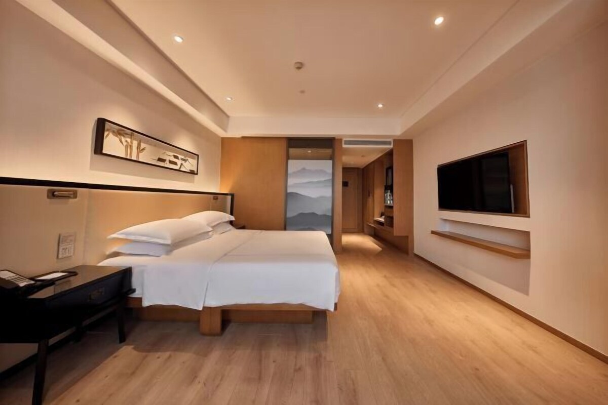 A modern hotel room with a bed, bedside table, TV, and artwork on the wall.