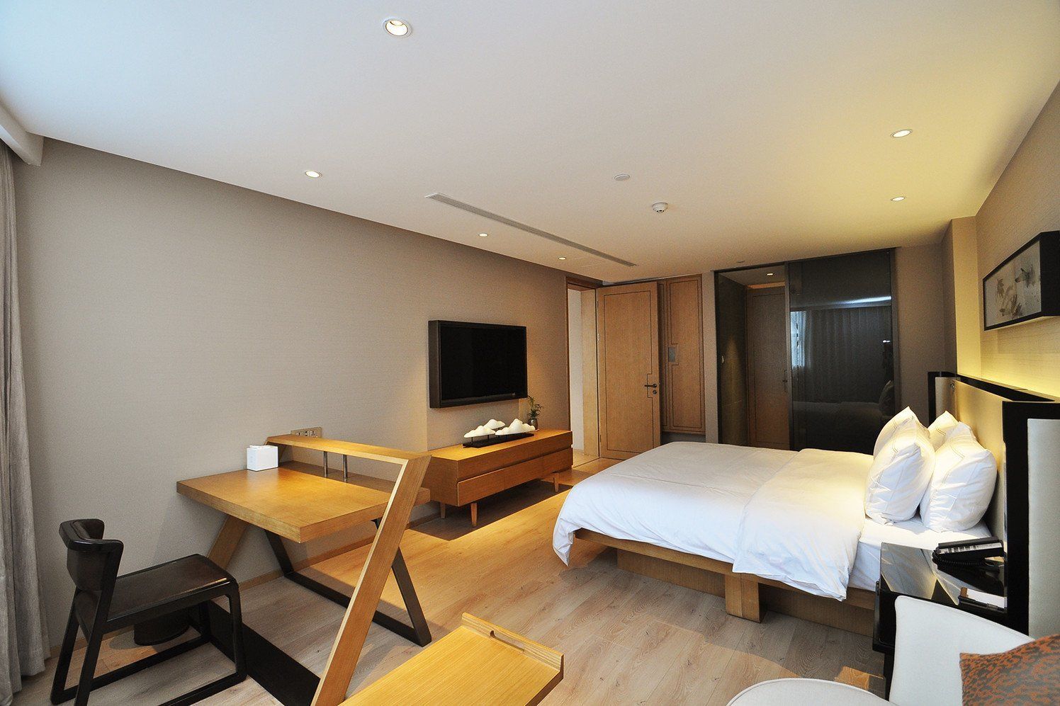 A modern hotel room with a bed, a desk, a chair, a TV, and a wardrobe.