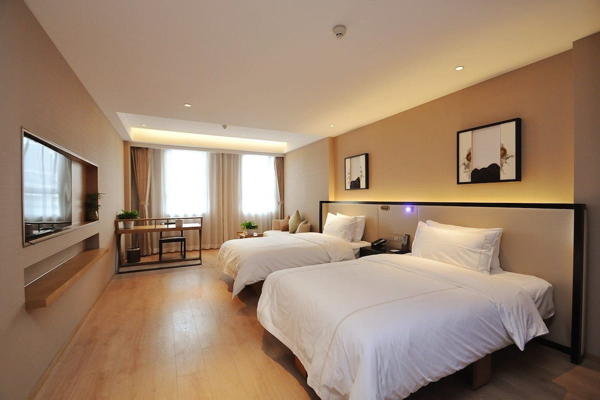 Quarto de hotel com duas camas, uma mesa e uma janela grande.