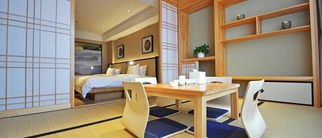 A traditional Japanese-style room with tatami flooring, a low wooden table, and a bed with white bedding.