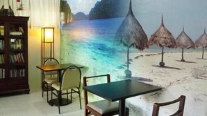A dining area with a mural of a beach scene, a table, chairs, a bookshelf, and a lamp. - Tarasa Hostel (Pasay)