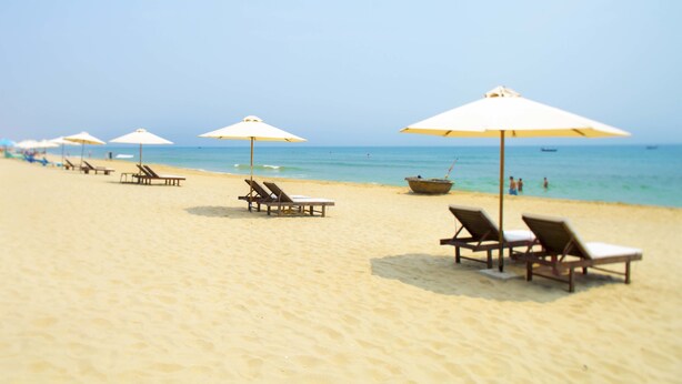 A beach with rows of sun loungers and umbrellas, a boat in the water, and a clear sky. - An Bang Beach Dolphin Homestay Hoi An (Da Nang)