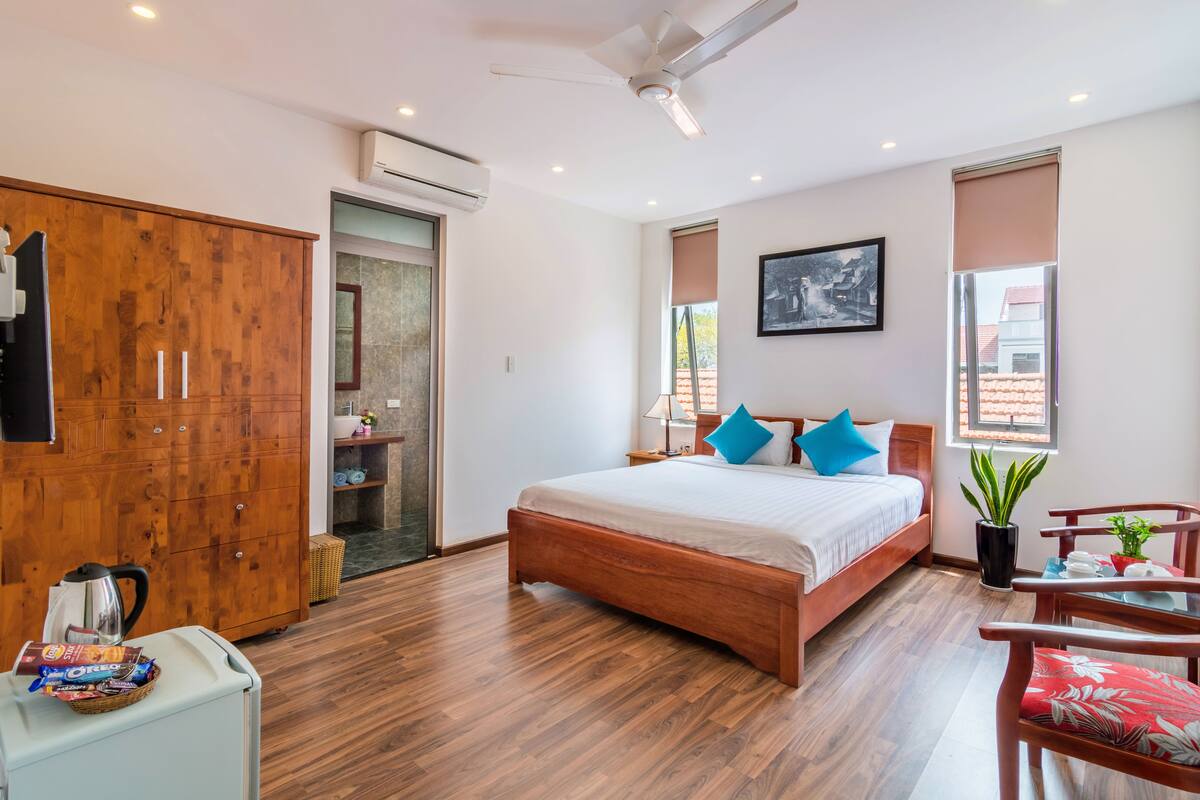 A modern bedroom with a wooden bed, a wardrobe, a desk with a chair, and a potted plant.