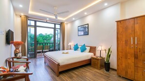 A bedroom with a bed, wooden wardrobe, bedside table, lamp, potted plant, and a view of the outdoors through a sliding door. - An Bang Beach Dolphin Homestay Hoi An (Da Nang)