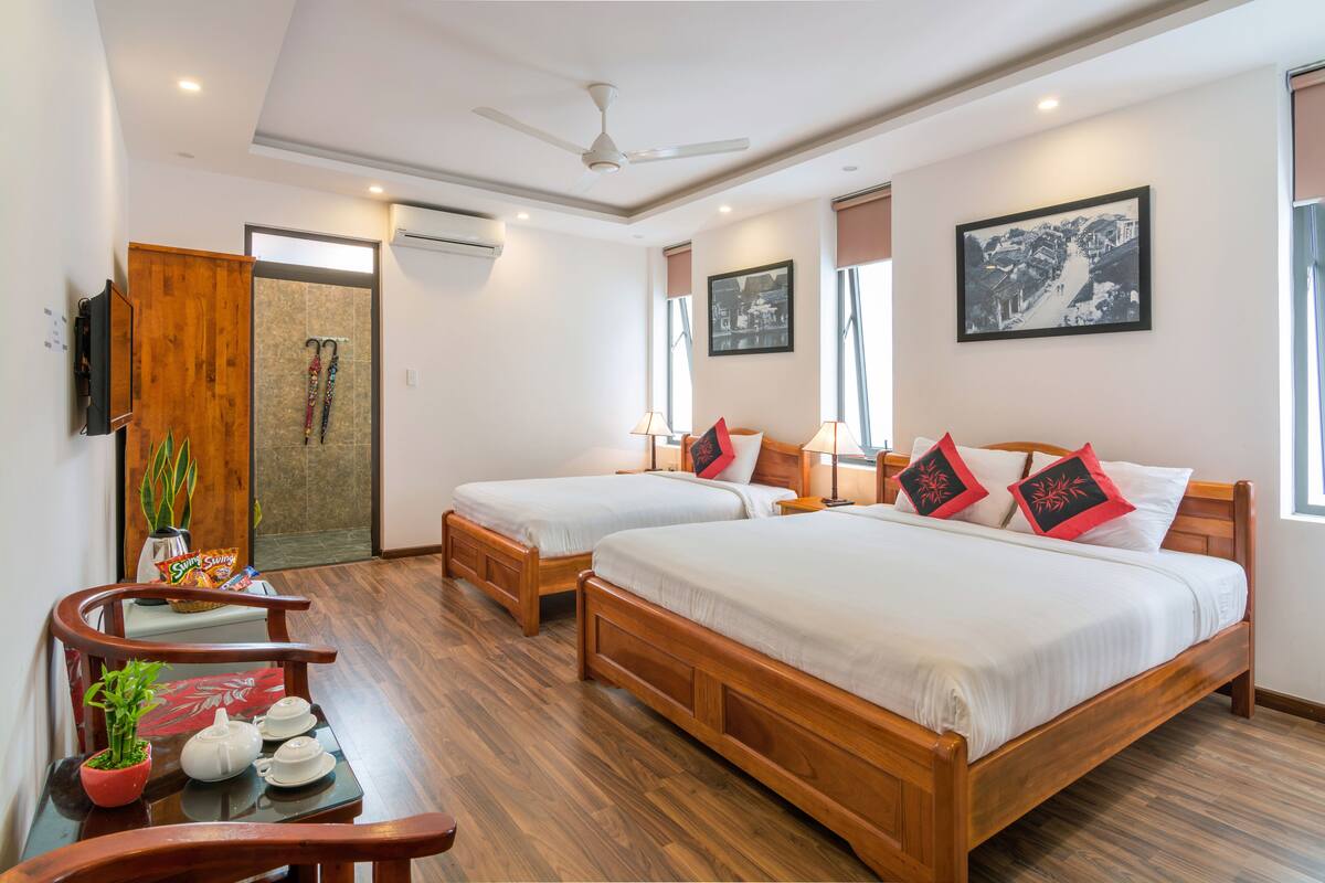 A hotel room with two wooden beds, a wooden desk with a potted plant, a television, and a framed picture on the wall.