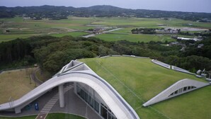 Un edificio moderno con techo curvo y un amplio campo verde al frente.
