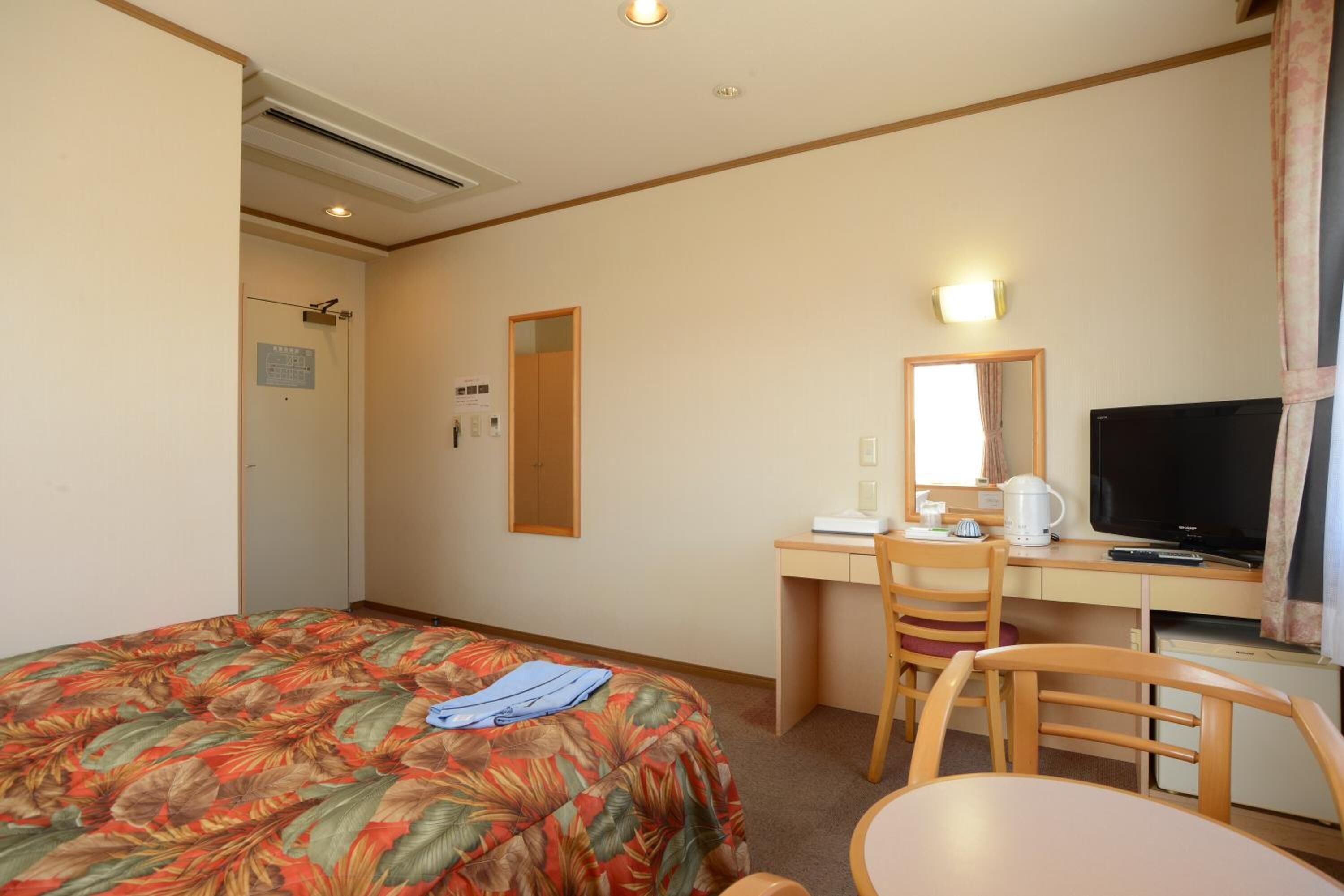 Una habitación de hotel con cama, escritorio con silla, televisor y espejo.