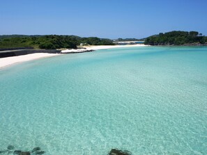 A beach with clear turquoise water, white sand, and a forested hill in the background. - Iki Marina Hotel (Iki)
