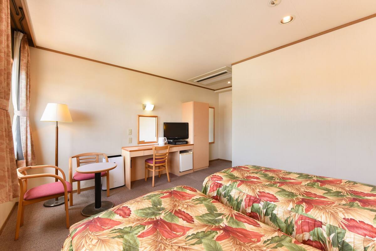 A hotel room with two beds, a desk with a chair, a television, and a small refrigerator.