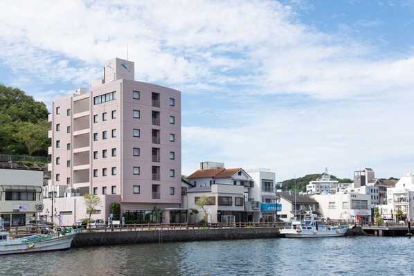 A waterfront building with multiple floors, a dock with boats, and a clear sky. - Iki Marina Hotel (Iki)