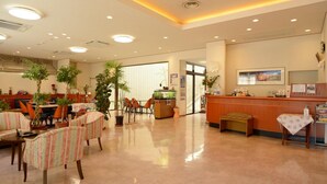 Un vestíbulo de hotel con mostrador de recepción, zona de estar con sillas a rayas y plantas en macetas.