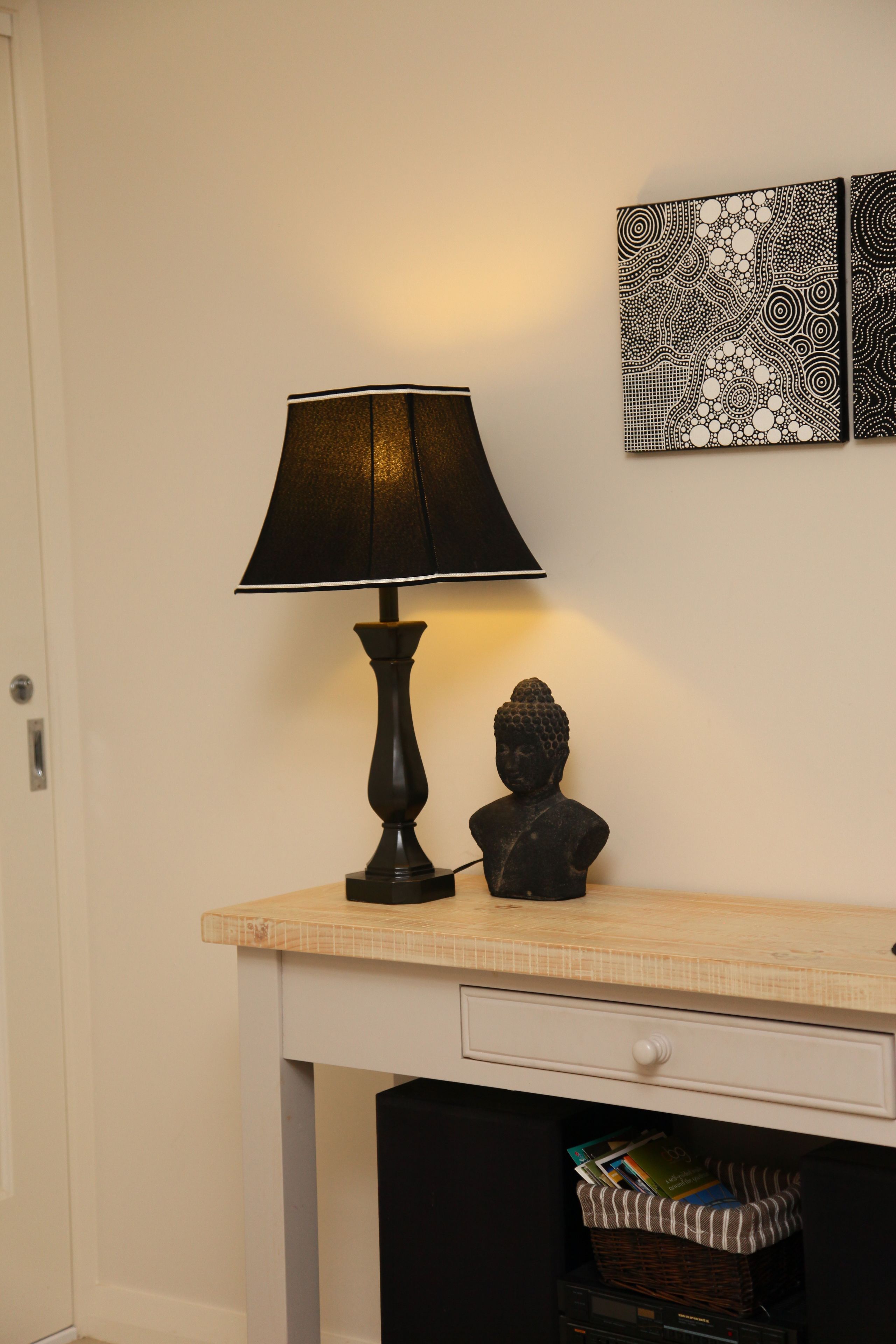 Un escritorio con una lámpara negra, un busto y una pared decorada con motivos artísticos.