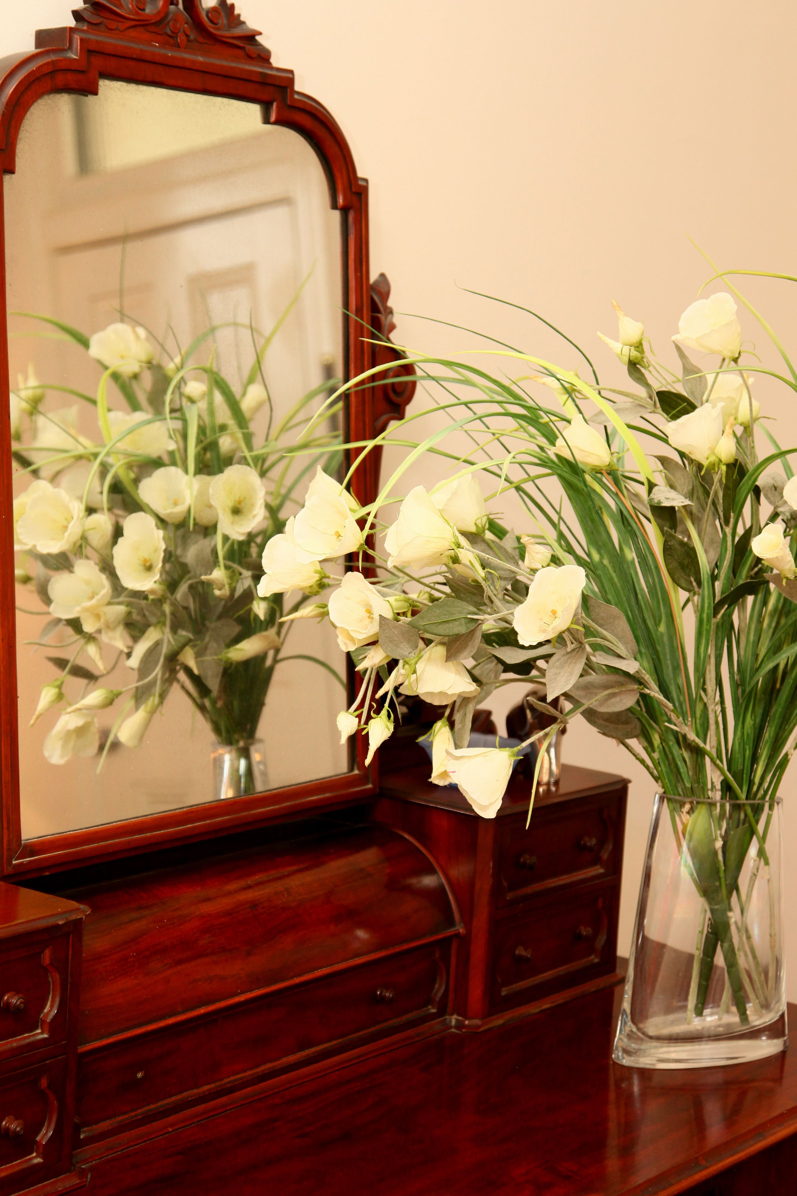 Un aparador de madera con espejo y dos jarrones de flores blancas.
