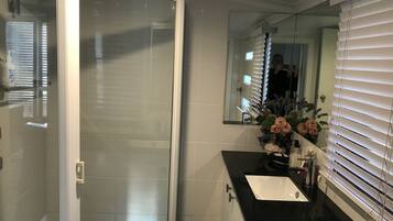 A bathroom with a glass shower door, a white sink, and a mirror with a floral arrangement.