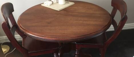 A round wooden dining table with four chairs, a vase with flowers, and a placemat on the table.