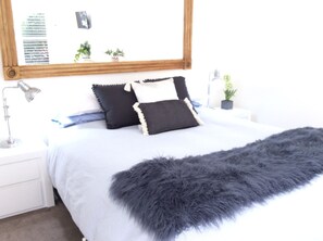 A neatly made bed with a fluffy grey throw, a bedside lamp, and a small potted plant on a white nightstand. - Apartments On The Park (Orange)