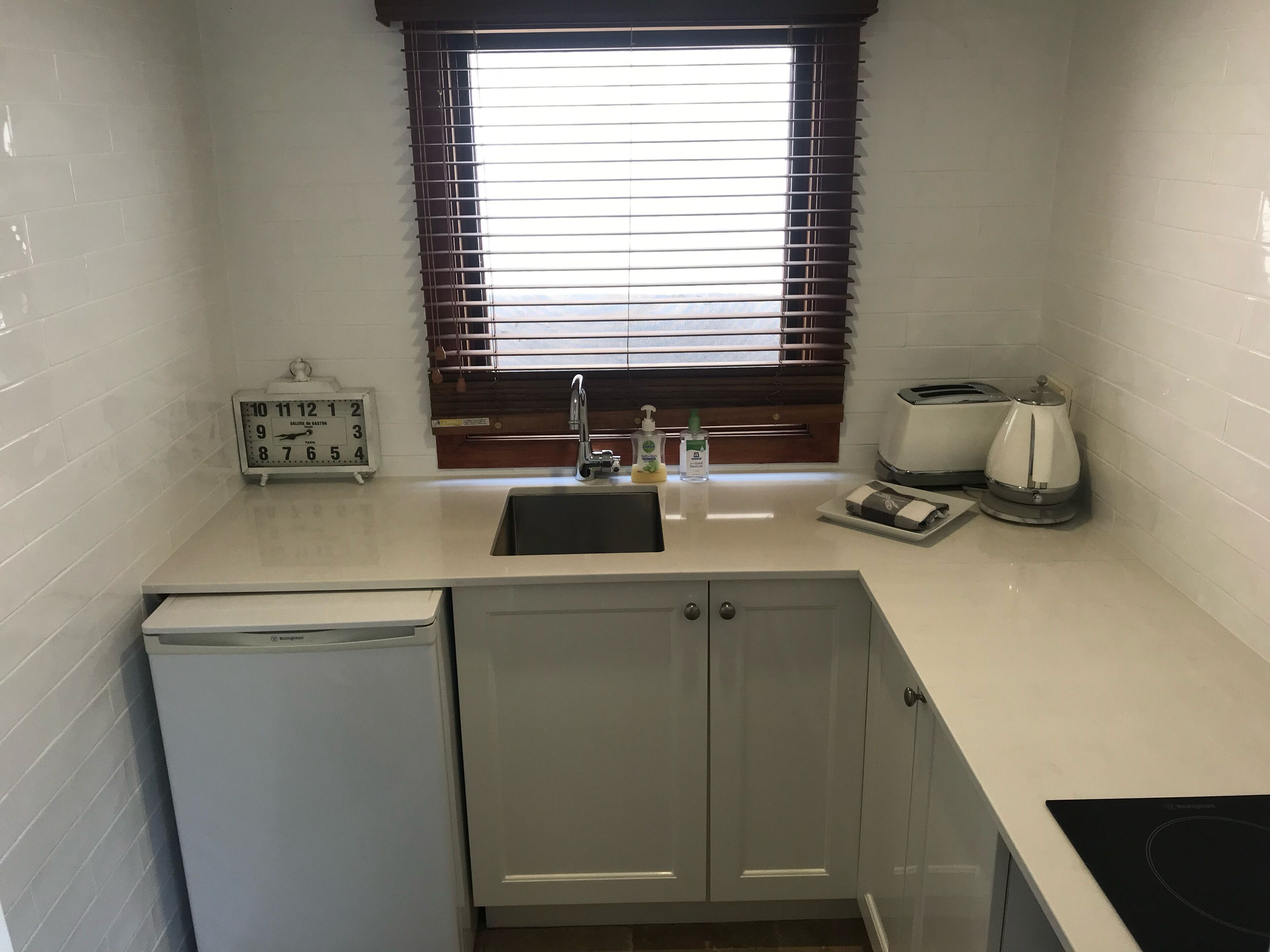 A compact kitchen with a sink, a clock, a toaster, and a coffee maker.