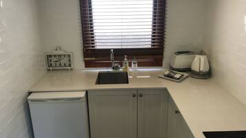 A compact kitchen with a sink, a clock, a toaster, and a coffee maker.