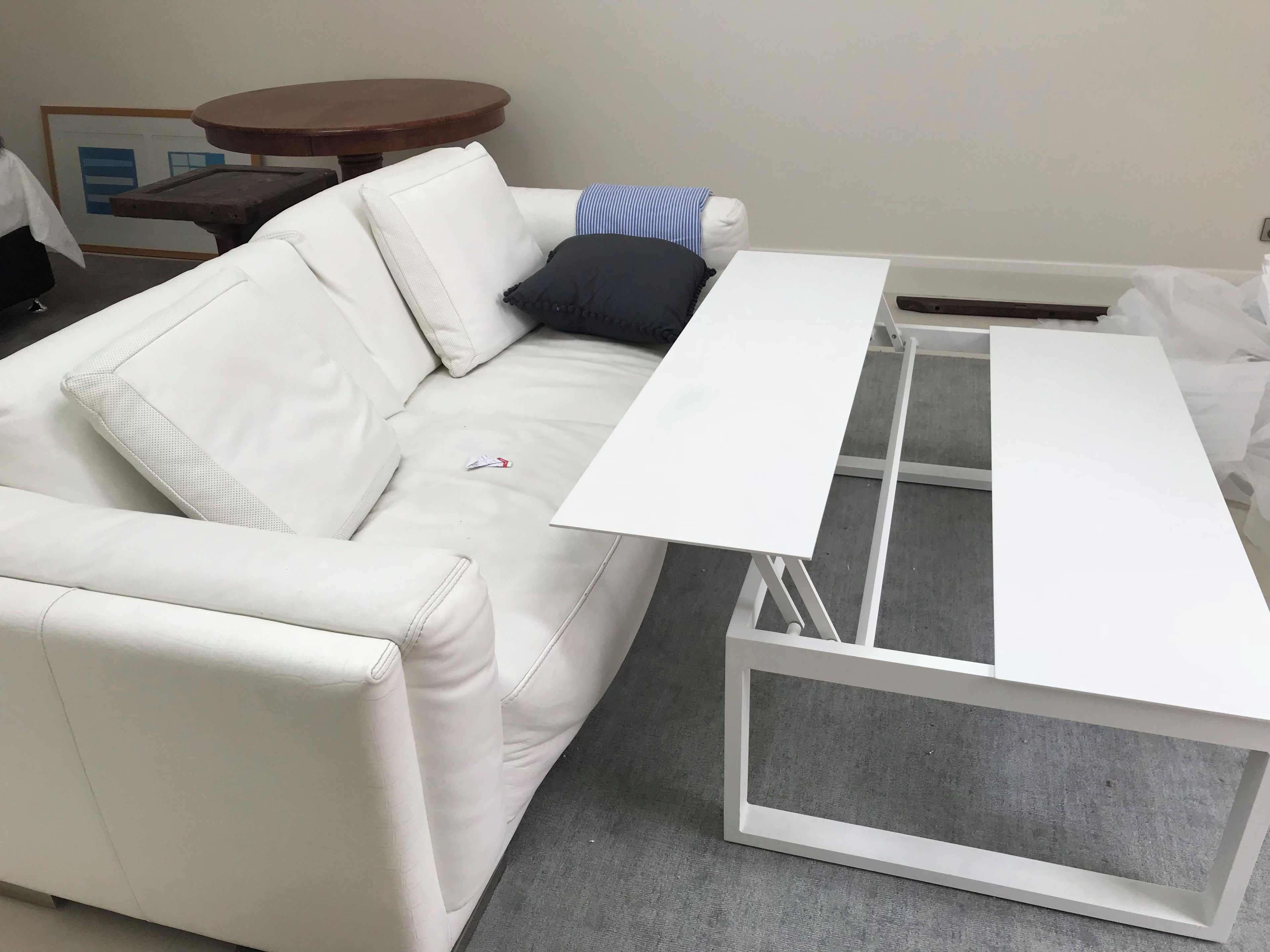 A white leather sofa with a white table and a small round wooden table in a room.
