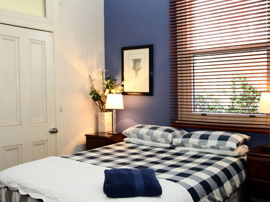 A neatly made bed with a checkered bedspread, a blue towel, and a framed picture on the wall.