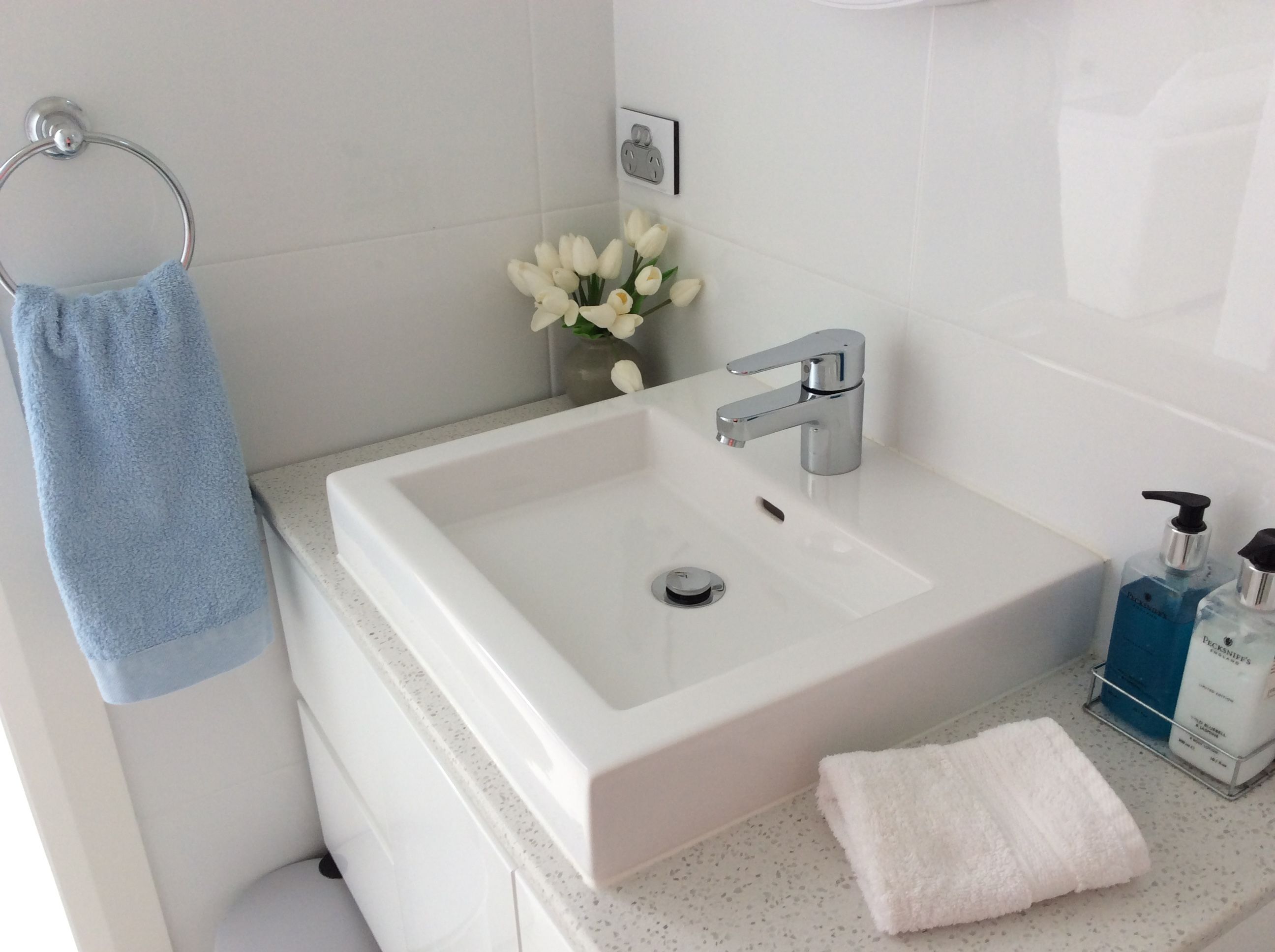 Een badkamer met een wit wastafel, een blauwe handdoek, een witte handdoek en een vaas met witte bloemen.