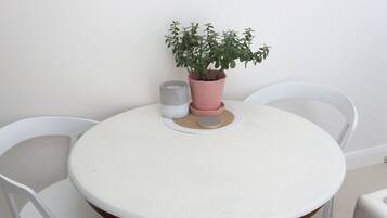 Una mesa redonda blanca con base de madera, rodeada de sillas blancas, y una planta en maceta sobre la mesa.