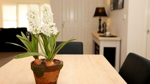 Ein Blumentopf mit weißen Blüten auf einem Holztisch in einem Raum, im Hintergrund eine Tür und eine Lampe.