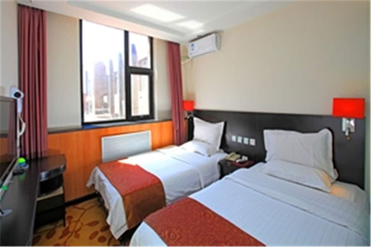 Habitación de hotel con dos camas, un escritorio, un televisor y una ventana con cortinas.