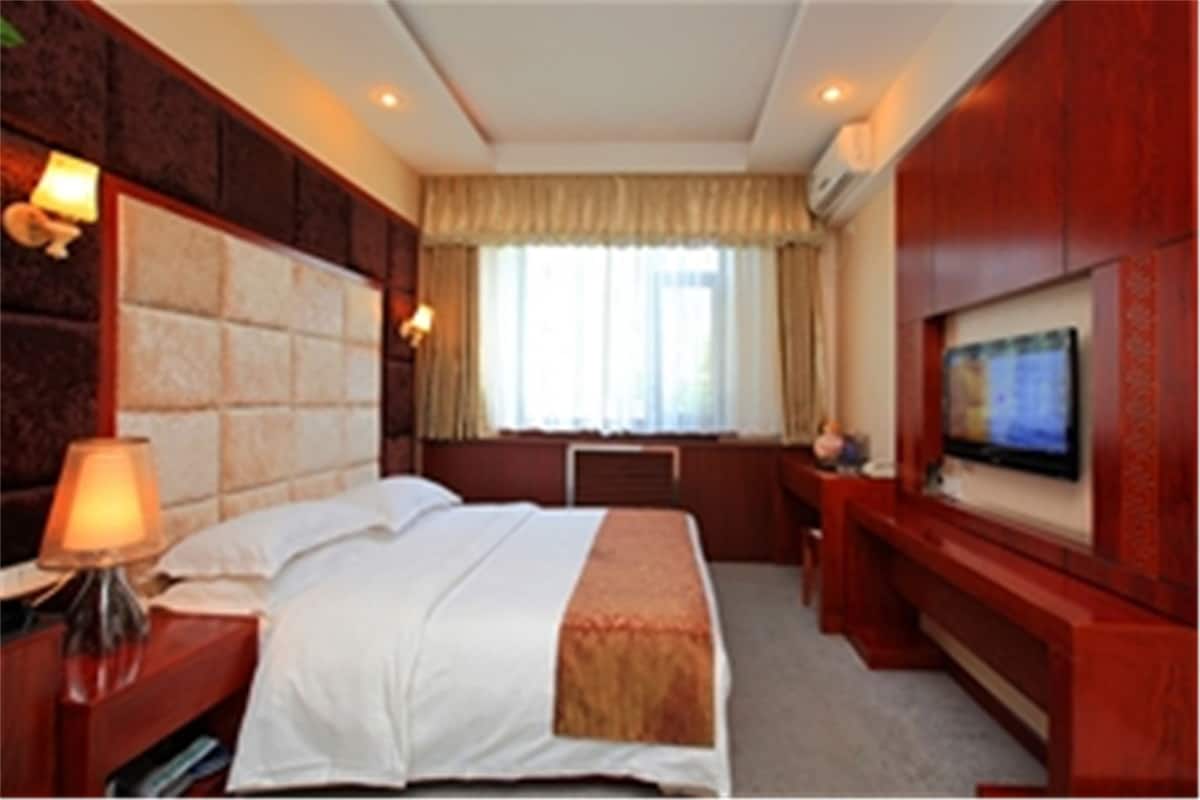 Una habitación de hotel con una cama grande, un escritorio con una silla, un televisor y un ventanal con cortinas.