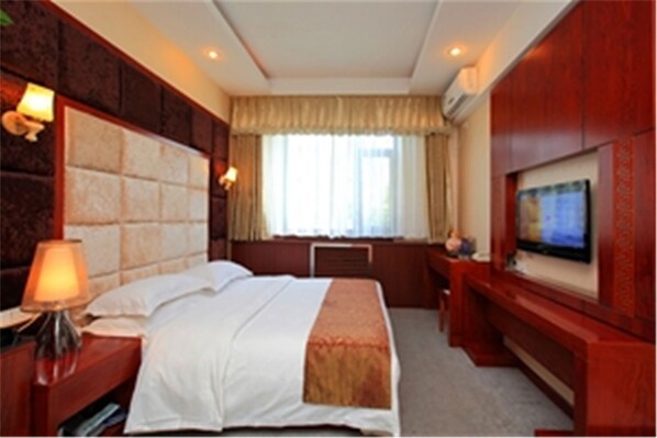 Una habitación de hotel con una cama grande, un escritorio con una silla, un televisor y un ventanal con cortinas.