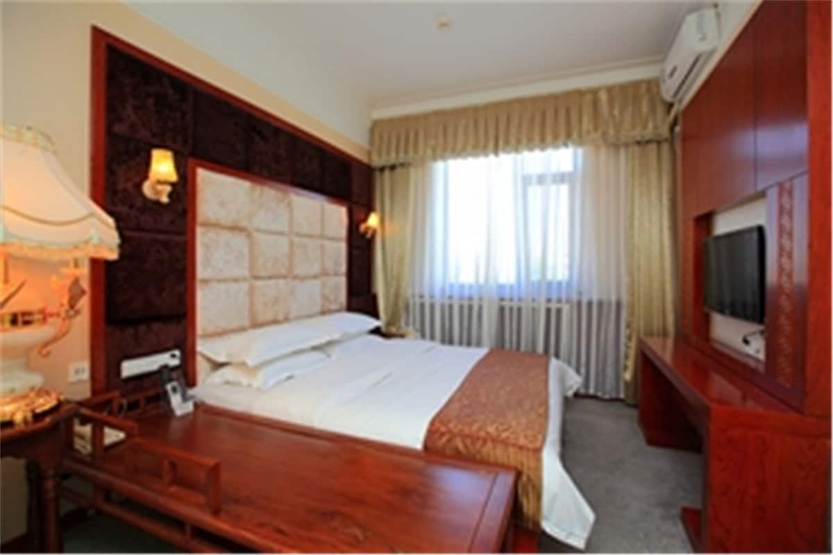 Habitación de hotel con una cama grande, cabecera de madera, escritorio, silla, televisor y ventana con cortinas.