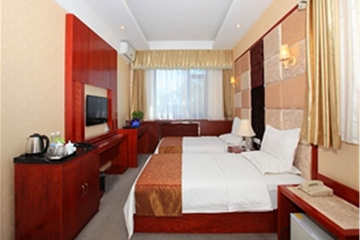 Una habitación de hotel con cama, escritorio, televisor, teléfono y ventana con cortinas.