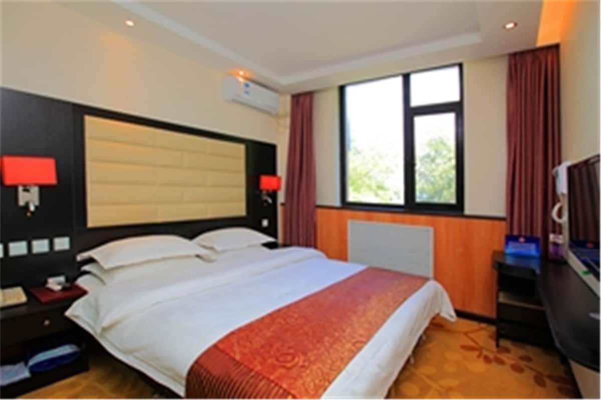 Una habitación de hotel con una cama grande, una mesita de noche con lámpara, un escritorio con computadora y una ventana con cortinas.